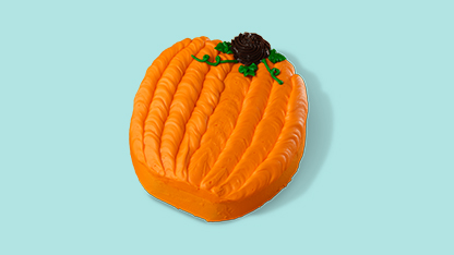 An orange pumpkin-shaped cookie decorated like a jack o'lantern with a green stem and eyes.