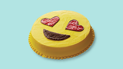 A cake decorated with a face of emojis, placed on a blue surface.